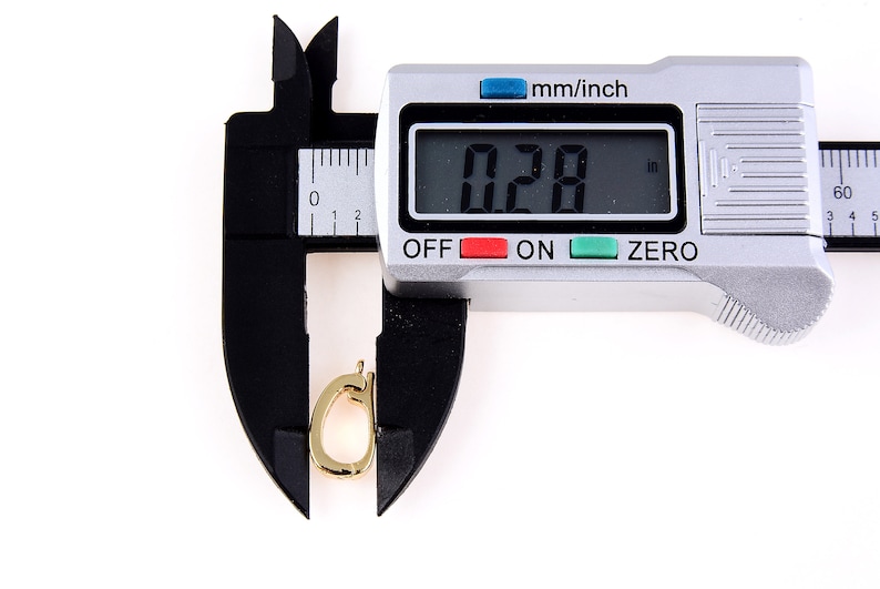 May include: A silver digital caliper measuring a gold-colored metal object. The caliper display reads "0.28 in".
