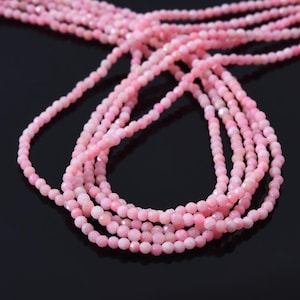 May include: A strand of pink gemstone beads. The beads are faceted and have a light pink color. The beads are strung on a clear thread and are arranged in a loose, flowing pattern.