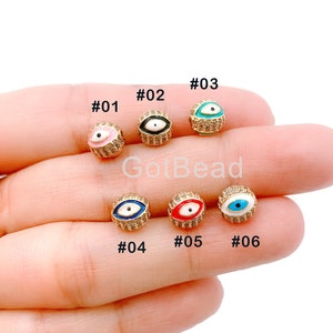 May include: Six gold-toned evil eye beads with different colored enamel accents. The beads are numbered #01 through #06. Each bead has a white enamel eye with a black pupil and is surrounded by clear rhinestones.