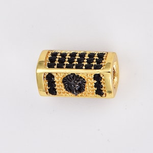 K&ouml;nnte beinhalten: Goldfarbene Perle mit einem schwarzen L&ouml;wenkopfdesign und schwarzen Zirkonia-Steinen.