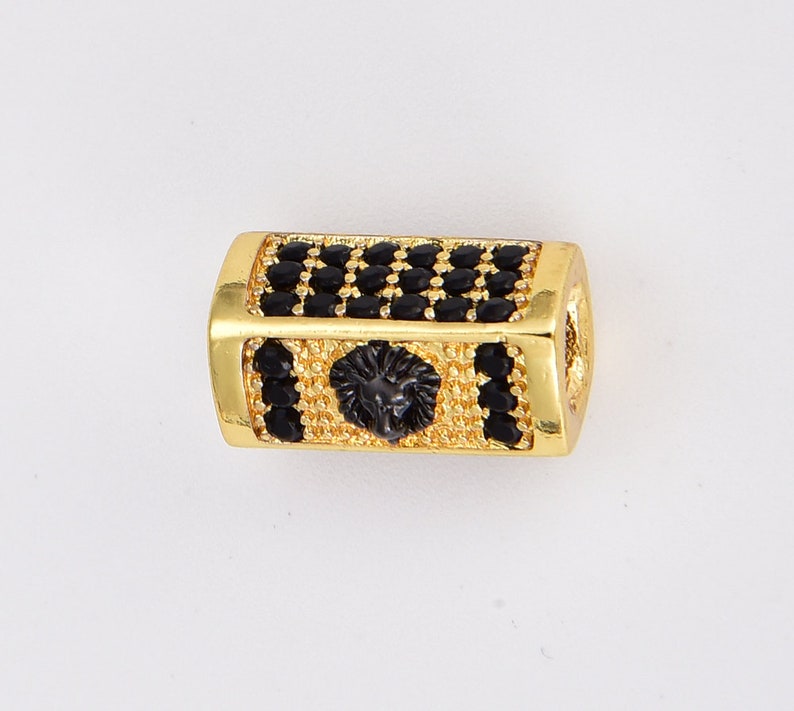 K&ouml;nnte beinhalten: Goldfarbene Perle mit einem schwarzen L&ouml;wenkopfdesign und schwarzen Zirkonia-Steinen.