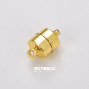 May include: Gold-toned magnetic clasp for jewelry making. The clasp is cylindrical with a smooth, shiny finish. It has a small loop on one end and a magnetic closure on the other.
