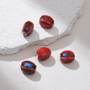 Peut inclure: Cinq perles en céramique rouge brillant. Chaque perle présente un accent bleu foncé et marron. Les perles sont de forme ovale et percées d'un trou en leur centre, idéal pour l'enfilage. Ces perles sont idéales pour la création de bijoux.