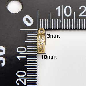 May include: Gold-toned metal pendant with clear cubic zirconia stones. The pendant measures 10mm in length and 3mm in width.