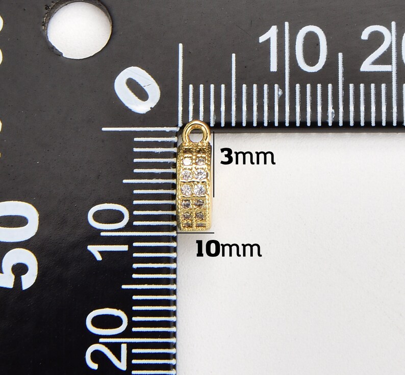 May include: Gold-toned metal pendant with clear cubic zirconia stones. The pendant measures 10mm in length and 3mm in width.