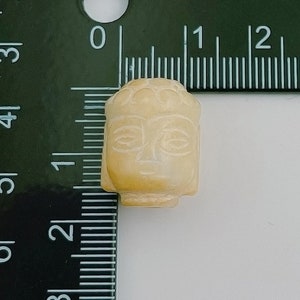 以下が含まれることがあります： クリーム色の小さな石製の仏陀の頭部のビーズ。ビーズは直径約2.5cmで、仏陀の顔の細かな彫刻が施されています。