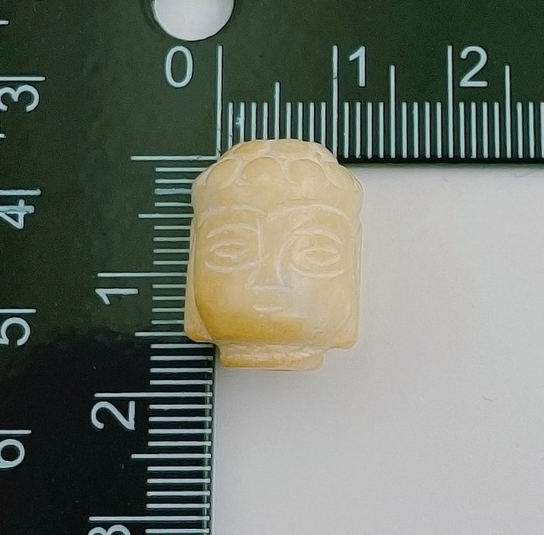 以下が含まれることがあります： クリーム色の小さな石製の仏陀の頭部のビーズ。ビーズは直径約2.5cmで、仏陀の顔の細かな彫刻が施されています。