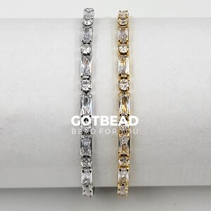 May include: Two silver and gold bracelets with clear cubic zirconia stones. The bracelets are on a white surface. GOTBEAD Bead for You is printed on the surface.
