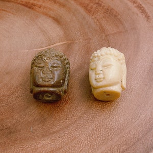 以下が含まれることがあります： 石で彫られた小さな仏陀の頭部の彫刻が2つあります。1つは茶色で、もう1つは白です。