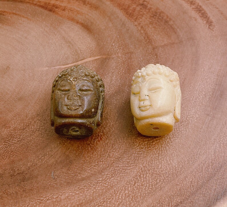 以下が含まれることがあります： 石で彫られた小さな仏陀の頭部の彫刻が2つあります。1つは茶色で、もう1つは白です。