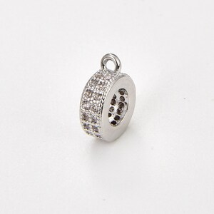 May include: Silver-toned round pendant with a clear crystal embellishment. The pendant has a loop at the top for attaching to a chain or cord.
