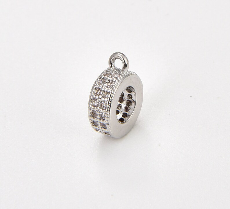 May include: Silver-toned round pendant with a clear crystal embellishment. The pendant has a loop at the top for attaching to a chain or cord.