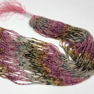 May include: A long strand of small, faceted, multicolored tourmaline beads in shades of pink, green, brown, and clear. The beads are strung on multiple threads and gathered at one end with a pink tassel tied with a silver-colored wire.