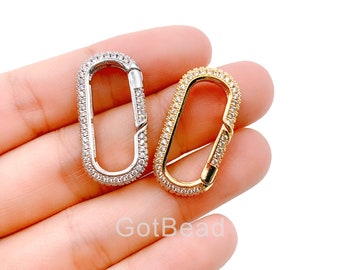 Könnte beinhalten: Zwei ovale Verschlüsse in Silber und Gold mit klaren Strasssteinen. Die Verschlüsse befinden sich auf einer Hand.