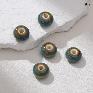 May include: Five ceramic beads. Each bead is a small, round shape with a hole through the center. The beads have a teal base color with a speckled texture, a brown band, and a white center. The number "#17" is in the upper right corner.