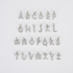 May include: A set of 26 silver charm pendants, each featuring a letter of the alphabet adorned with sparkling clear rhinestones. The charms are perfect for adding a personalized touch to necklaces, bracelets, or keychains.