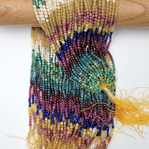 May include: A strand of gemstone beads in various colors, including turquoise, yellow, pink, blue, and white. The beads are strung on a thin wire and have a tassel at the end.