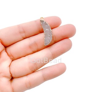 May include: A white agate crescent moon pendant with a gold-toned bail. The pendant is approximately 1.5 inches long and 1 inch wide.