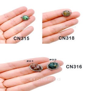 May include: Three oval-shaped connector charms with a silver-tone metal setting and a clear stone with a green, brown, and blue pattern. The charms are labeled #01, #02, and CN316.