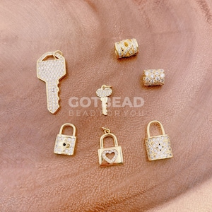 May include: A set of gold-tone charm pendants featuring a key, lock, and heart designs. Each charm is encrusted with clear rhinestones.