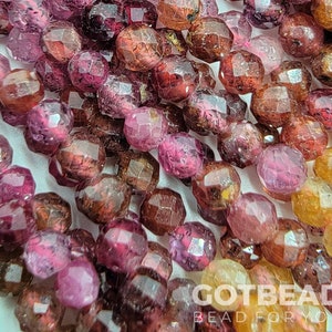 May include: A strand of faceted gemstone beads in shades of pink, orange, and brown. The beads are all approximately the same size and have a smooth, polished finish.