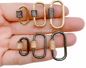Könnte beinhalten: Fünf ovale Verschlüsse in verschiedenen Größen mit einem zylindrischen Abschnitt in der Mitte. Die Verschlüsse sind aus goldenem und schwarzem Metall gefertigt und mit klaren Strasssteinen verziert.
