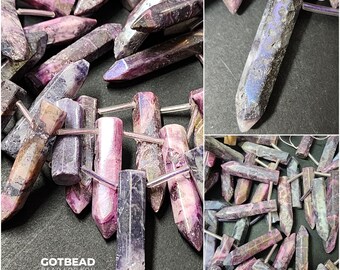 Op de afbeelding: Een close-up van een stapel paarse en roze edelsteen kralen met zilveren metalen dopjes. De kralen zijn gevormd als lange, dunne punten. De kralen zijn in een stapel gerangschikt, waarbij sommige kralen elkaar overlappen. De kralen zijn allemaal van verschillende groottes en vormen. De tekst "GOTBEAD BEAD FOR YOU" is zichtbaar in de linkerbenedenhoek van de afbeelding.