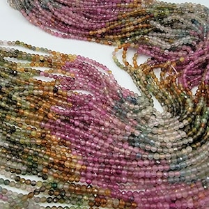 May include: A collection of multi-colored tourmaline gemstone beads arranged in multiple strands. The small, faceted, round beads display a gradient of pink, green, yellow, and blue hues, strung together on a thin, light-colored thread.