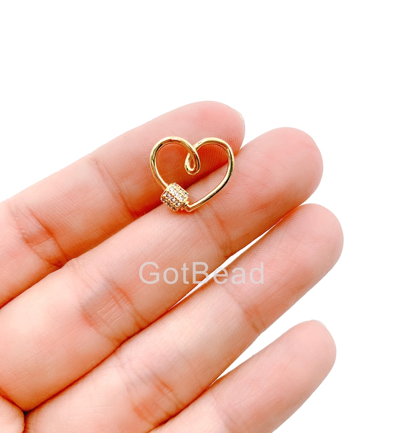 May include: Gold heart-shaped charm with a clear crystal-encrusted bead. The charm is a connector for jewelry making.