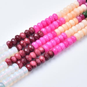 May include: A collection of faceted round beads arranged in parallel strands. The beads feature a gradient of colors including translucent white, deep burgundy, vibrant magenta, and soft peach, creating a multi-colored pattern of gemstone-like units.