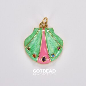 Op de afbeelding: Een gouden schelpbedel met groen en roze emaille en kleurrijke strass steentjes. De bedel heeft een lus aan de bovenkant om aan sieraden te bevestigen.