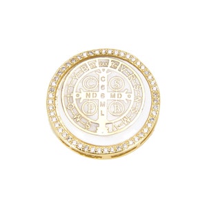 May include: A gold-colored pendant with a white center featuring an intricate design and text. The outer edge is lined with small, clear gemstones. The pendant is round and has a religious theme.