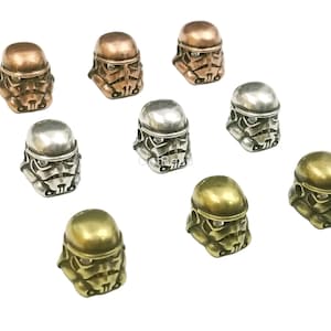Puede incluir: Diez abalorios de metal en forma de casco de Stormtrooper de Star Wars. Los abalorios son de tres colores diferentes: plata, oro y cobre.