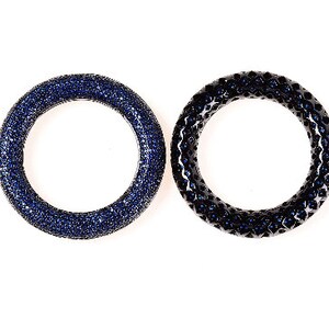 May include: Two circular rings, one a deep blue with a surface covered in small, sparkling stones. The other ring is black with a textured surface and blue stones. Both are set against a white background.