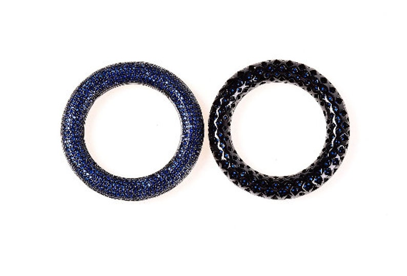 May include: Two circular rings, one a deep blue with a surface covered in small, sparkling stones. The other ring is black with a textured surface and blue stones. Both are set against a white background.