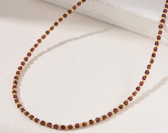 May include: A delicate gold chain necklace with small, dark red garnet beads.