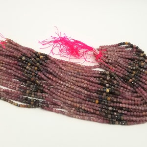 May include: A strand of pink, brown, and black gemstone beads. The beads are faceted and have a square shape. The beads are strung on a thin thread and are ready to be used for jewelry making.