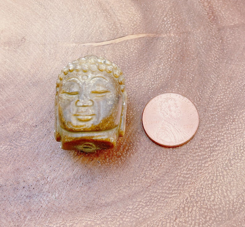 以下が含まれることがあります： 目を閉じた仏陀の頭部の小さな緑色の石の彫刻。彫刻は日本の1円玉と同じくらいの大きさです。