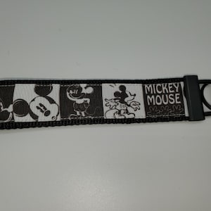 May include: Black and white Mickey Mouse key chain with a black strap and a silver metal ring. The strap has a repeating pattern of Mickey Mouse images and the text "Mickey Mouse".