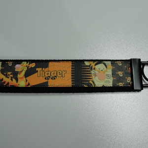 May include: Black and orange key chain with a Tigger character from Winnie the Pooh. The key chain has a black metal ring.