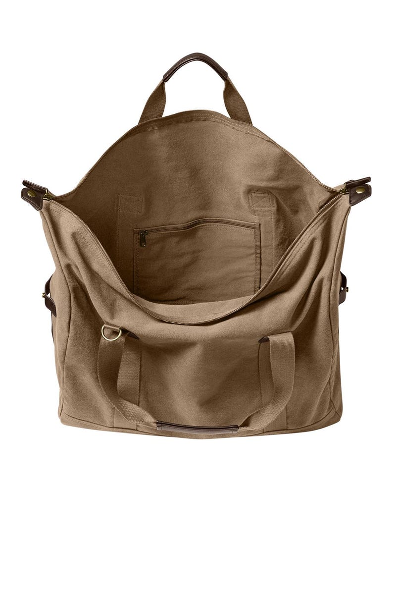 May include: A large, open-top tan canvas duffel bag featuring dark brown leather handle accents, a top zipper closure, and a single interior zippered pocket. The bag includes two sturdy fabric handles and side metal hardware for strap attachments.