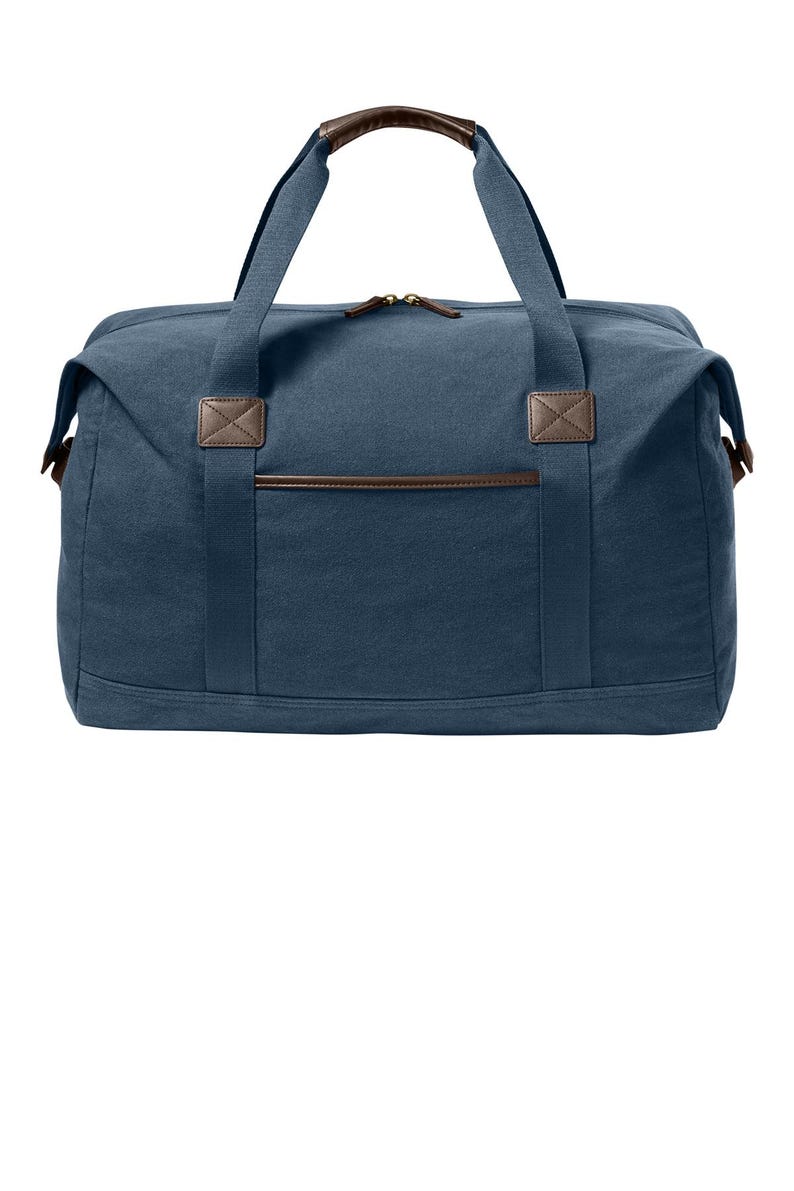 May include: A navy blue canvas duffel bag featuring brown faux leather accents on the handles, zipper pulls, and front pocket trim. The bag includes two top handles, a main zippered compartment, and a rectangular front pocket with stitched detailing.