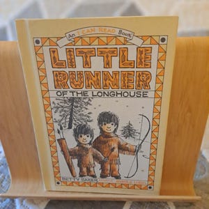 May include: A vintage children's book titled Little Runner of the Longhouse, an I Can Read Book by Betty Baker with illustrations by Arnold Lobel. The cover features a yellow and orange border with a black and white drawing of two children.