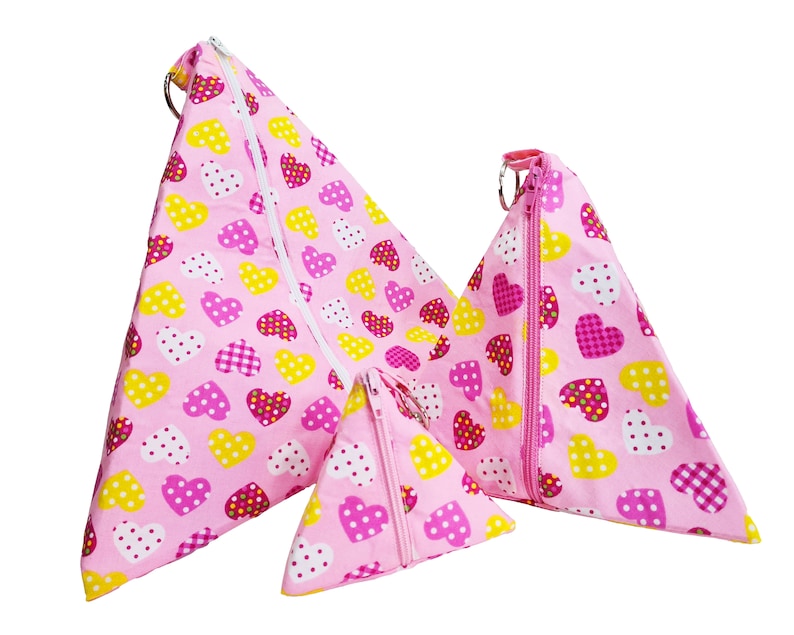 Pode incluir: Tr&ecirc;s bolsas de z&iacute;per de forma triangular rosa com um padr&atilde;o de cora&ccedil;&atilde;o. As bolsas s&atilde;o feitas de tecido e t&ecirc;m um fecho de correr. A bolsa maior tem um anel na parte superior.
