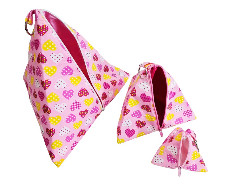 Pode incluir: Tr&ecirc;s bolsas de z&iacute;per cor-de-rosa com um padr&atilde;o de cora&ccedil;&otilde;es em tons de rosa, amarelo e branco. As bolsas s&atilde;o de tamanhos diferentes e est&atilde;o abertas para mostrar o forro rosa.