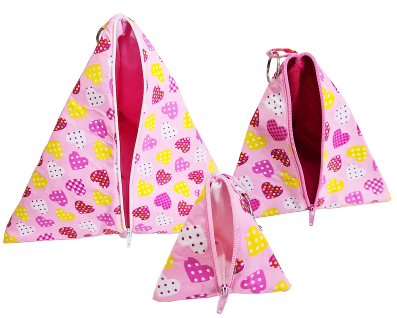 Pode incluir: Tr&ecirc;s bolsas de z&iacute;per triangulares cor-de-rosa com um padr&atilde;o de cora&ccedil;&atilde;o. As bolsas s&atilde;o de tamanhos diferentes e t&ecirc;m cora&ccedil;&otilde;es rosa e amarelos com bolinhas brancas.