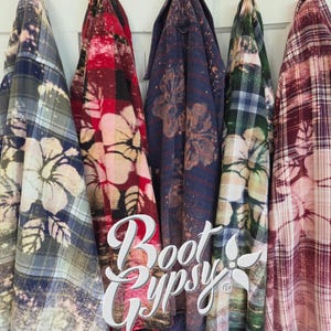 May include: Five long-sleeve button-down shirts with plaid patterns and bleached hibiscus flower designs in various colors including blue, red, dark blue, green, and maroon. The white text Boot Gypsy is overlaid on the shirts in a script font.