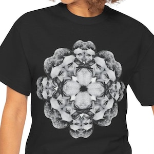 Op de afbeelding: Zwart T-shirt met een cirkelvormig ontwerp met een herhalend patroon van een mannengezicht. Het ontwerp is in grijstinten en wit.