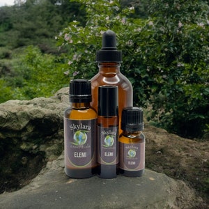May include: Three amber glass bottles of Skylara Essentials Elemi oil. The set includes a large dropper bottle, a medium roller bottle, and a small bottle, all featuring labels with a globe logo and the text Skylara Essentials and ELEMI.