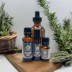 May include: Three amber glass bottles of Skylara Essentials Valerian Root oil. The largest bottle has a black dropper cap, while the two smaller bottles have black screw caps. Each bottle features a purple label with the brand logo and text.